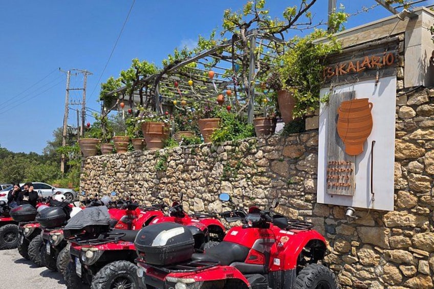 A row of red ATVs parked in front of a stone wall with a sign that reads 'ISKALARIO'. 4