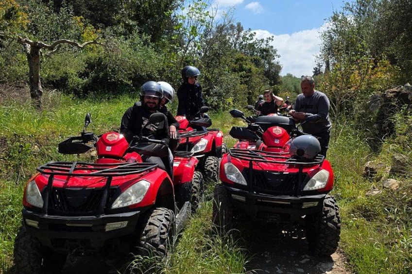 Four people on red all-terrain vehicles in a grassy area with trees and a clear sky. 3