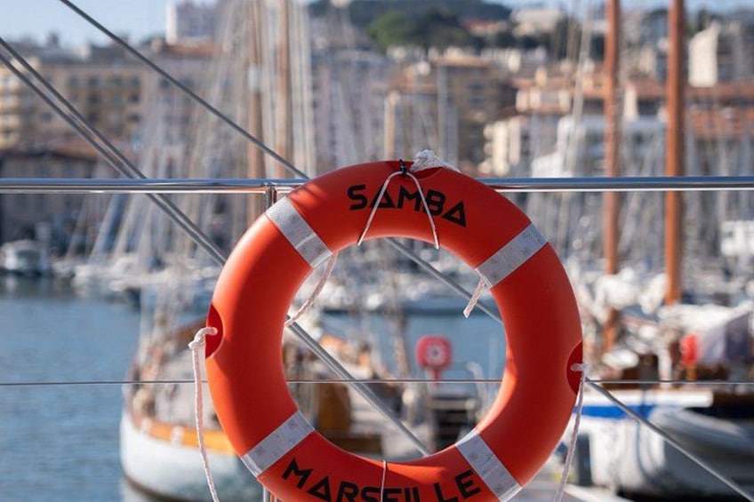 Un galleggiante con la scritta 'SAMBARA' e 'MARSIGLIA', un porto turistico con barche e edifici sullo sfondo. 2