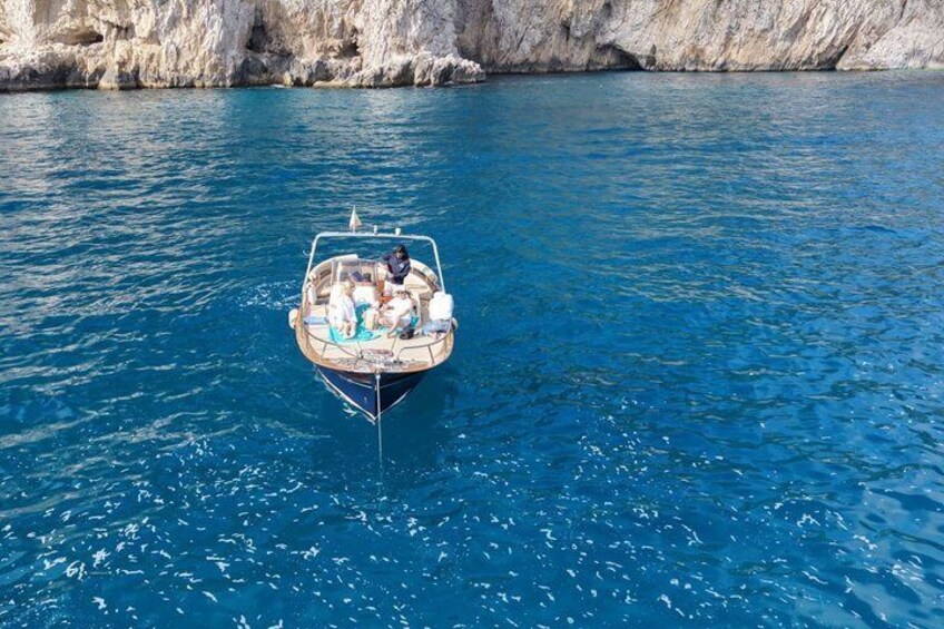 Un bateau avec des personnes à bord, naviguant sur une mer bleue et limpide, près d'une falaise rocheuse. 5