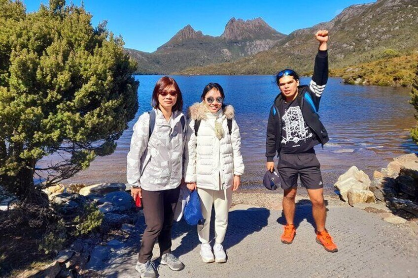Three people standing by a lake with mountains in the background. 4