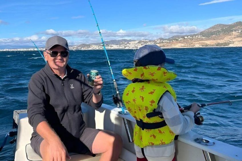 Two people fishing on a boat with a coastal landscape in the background. 1