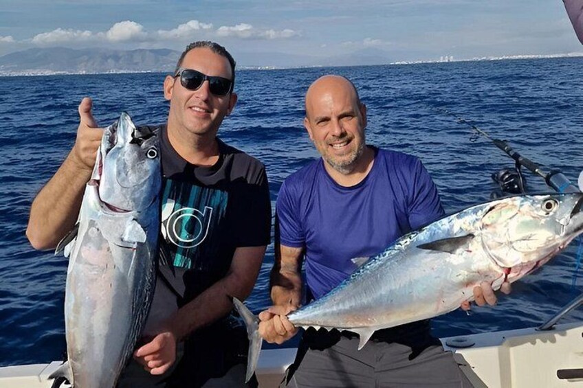 To personer holder fisk på en båd med vand og en fjer fjerntliggende kystlinje i baggrunden. 2