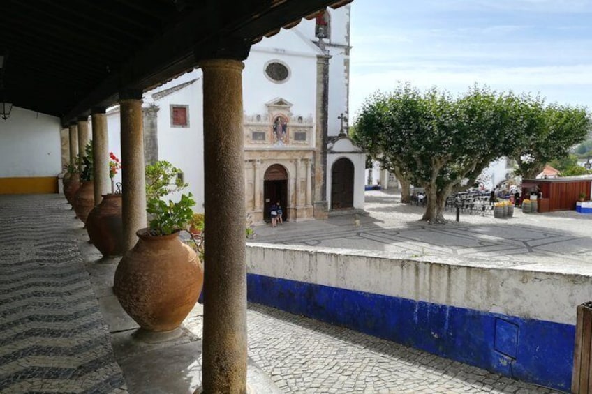 Une cour pavée de pierres, des pots en terre cuite, un bâtiment blanc doté d’un clocher et un arbre. 4