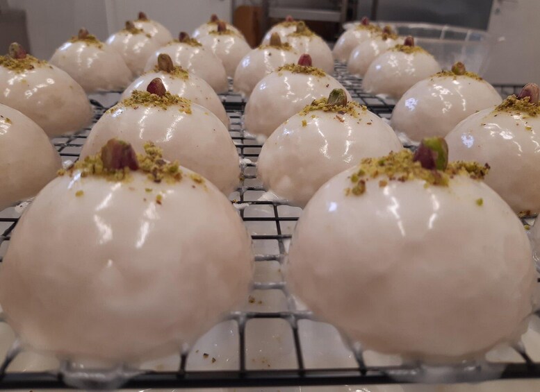 A tray of round, white pastries with a glossy finish, garnished with crushed nuts. 1