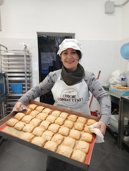 A person in a kitchen holding a tray of baked goods. 3