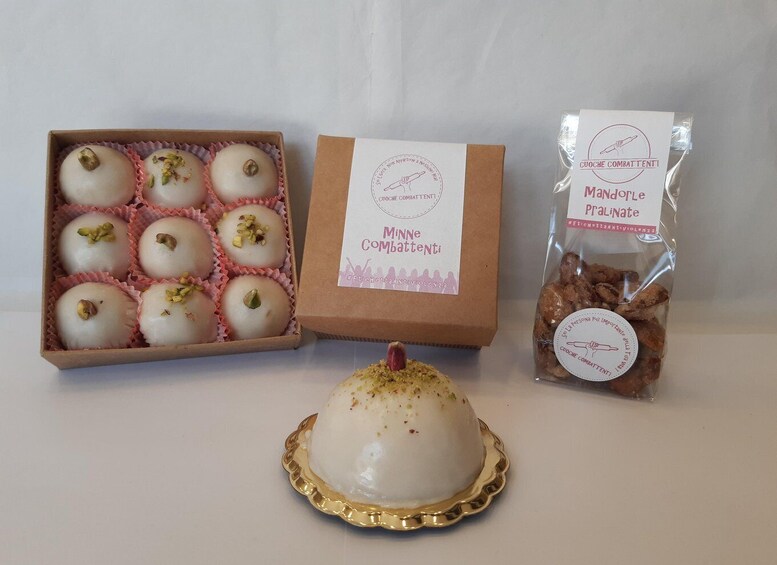 A box of white round pastries with pistachio garnish, a branded box with a logo, and a bag of cookies. 2