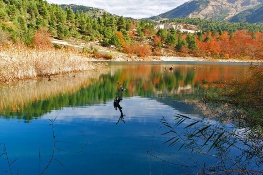 A calm lake with a person in a kayak, surrounded by autumn-colored trees and mountains in the background. 2