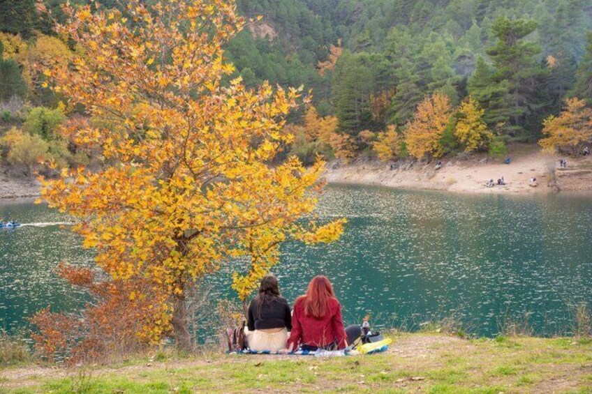 Two people sitting on a blanket by a lake with autumn foliage. 4