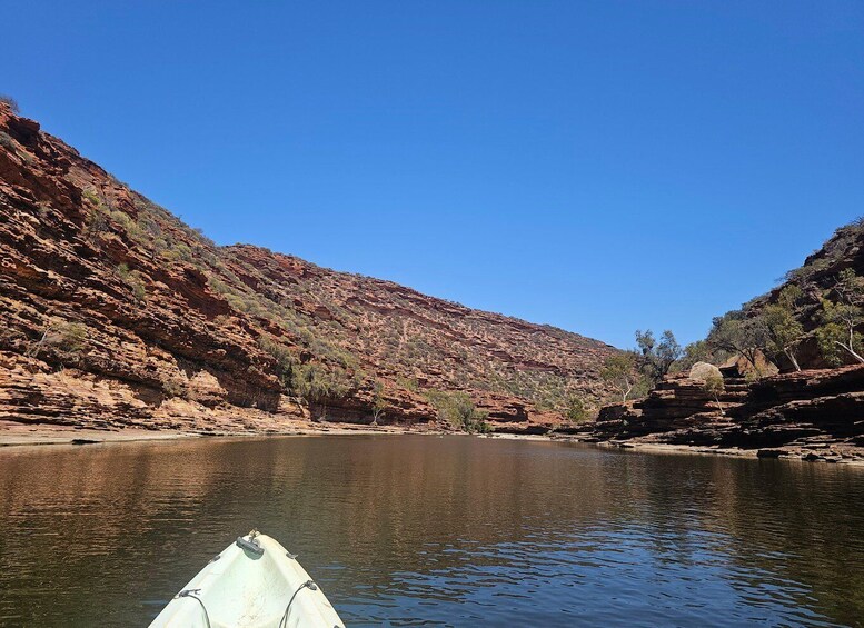 A calm river with a white boat in the foreground, surrounded by red rock cliffs and sparse vegetation. 2