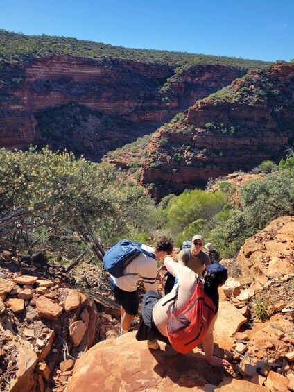 Hikers on a rocky trail with red cliffs and sparse vegetation in the background. 1