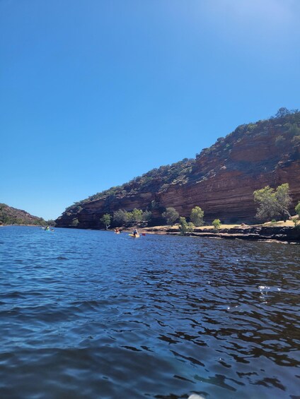A calm river with kayakers, surrounded by rocky cliffs and sparse vegetation. 5