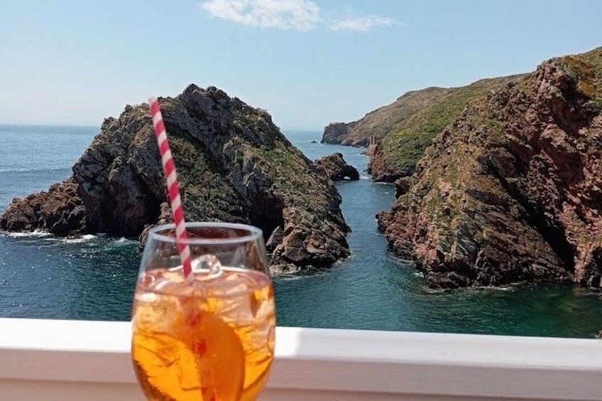 Un vaso de líquido color ámbar con una pajita a rayas, una costa rocosa y el océano. 2