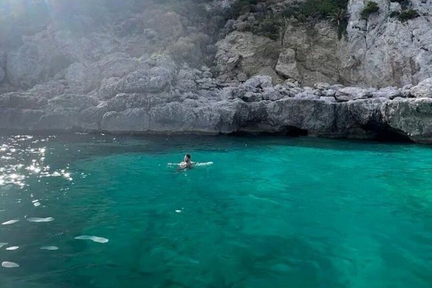 Una persona che nuota in acque turchesi limpide vicino a scogliere rocciose. 3