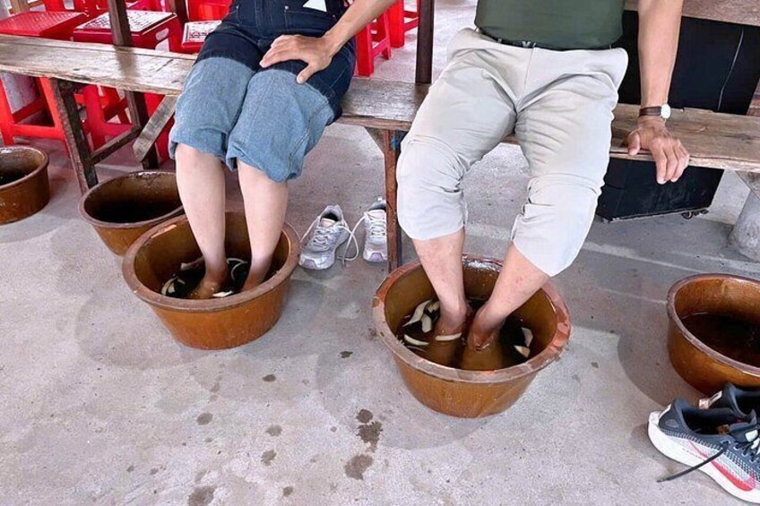 Deux personnes sont assises sur un banc, les pieds plongés dans de grands pots en argile. 3