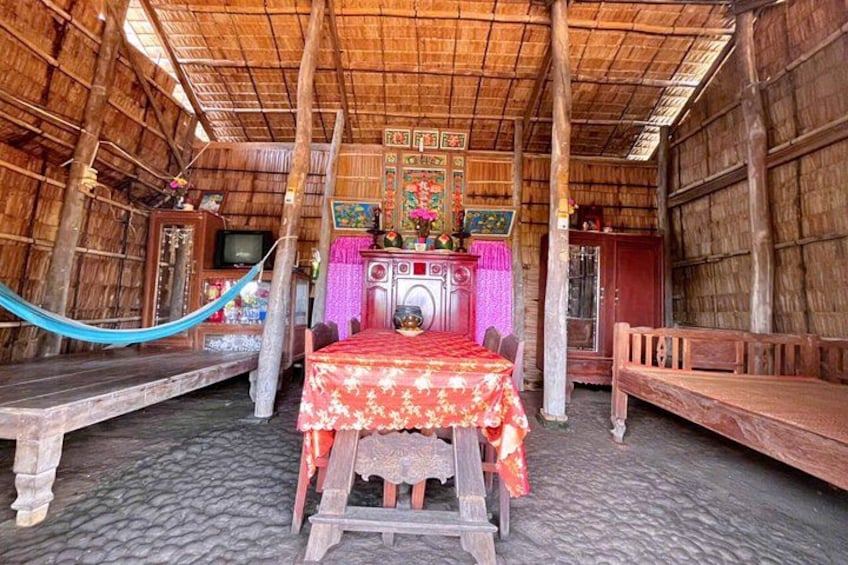 A traditional wooden hut with a thatched roof, a bed with a red floral bedspread, and a television on a wooden cabinet. 2