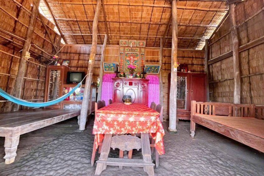 A traditional wooden hut with a thatched roof, a bed with a red floral bedspread, and a television on a wooden cabinet. 2