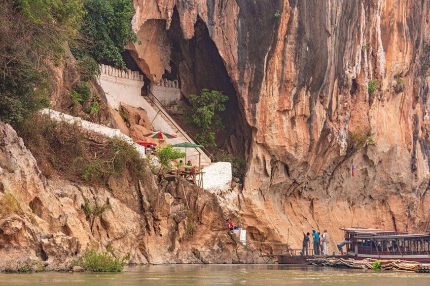 Une falaise rocheuse avec un escalier menant au sommet, un petit bateau sur l’eau et quelques personnes debout sur les marches. 1
