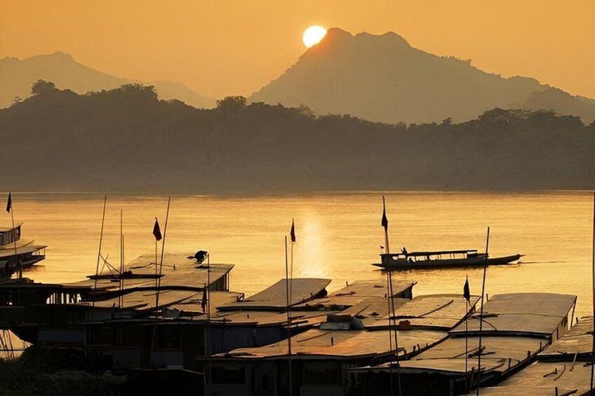Un coucher de soleil sur une étendue d’eau calme, avec des bateaux amarrés à un quai, et des montagnes en arrière-plan. 2