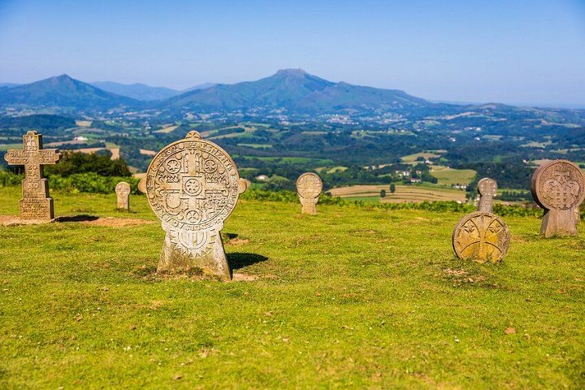 A cemetery with various stone crosses and headstones, set against a backdrop of rolling hills and distant mountains. 2