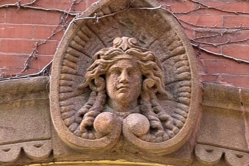 A stone carving of a face with curly hair and a halo, set in a brick wall with vines. 2