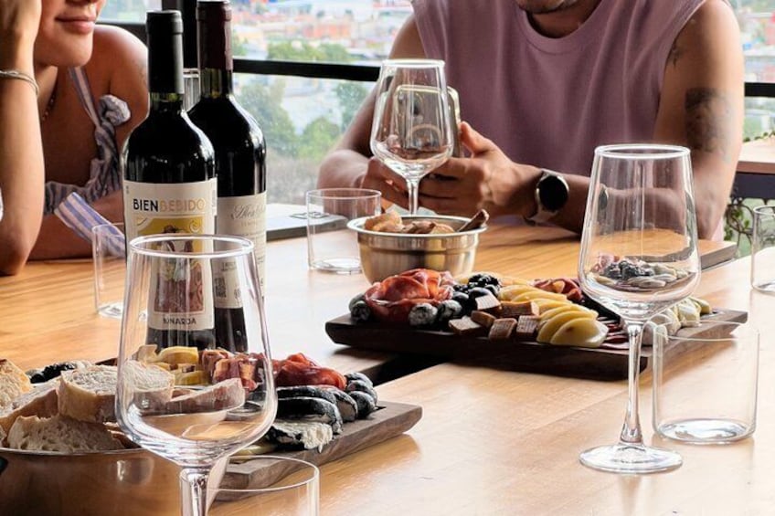 Una mesa con botellas de vino, copas y una tabla de embutidos. 3
