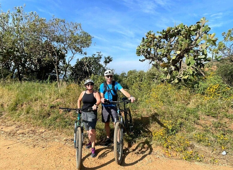 Two people on mountain bikes on a dirt trail with cacti and wildflowers in the background. 3