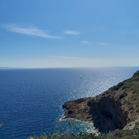 A coastal landscape with a clear sky, a rocky cliff, and a sailboat on the ocean. 3