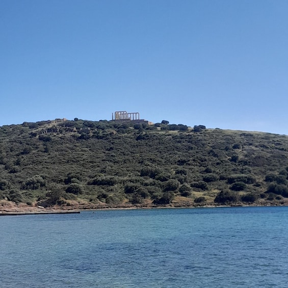 A hill with a structure resembling ancient ruins, dense green vegetation, and a body of water in the foreground. 4