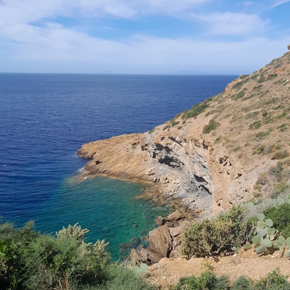 A coastal landscape with clear blue sea, rocky cliffs, and sparse vegetation. 5