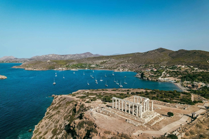 A coastal landscape with ancient ruins, clear blue sea, and sailboats. 1