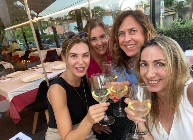 Four people toasting with wine glasses at an outdoor restaurant with tables set for dining. 1