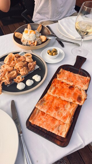 A meal with fried calamari, bread with salmon spread, and a glass of white wine on a table. 3