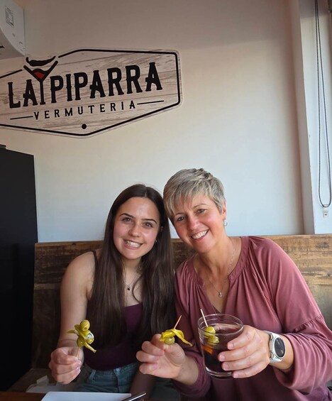Two people sitting at a table with a sign reading 'LAIPARRA VERMUTERIA' in the background. 2