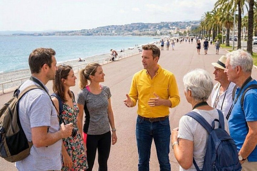 Un groupe de personnes se tient sur une promenade en bord de mer, avec des palmiers et une plage en arrière-plan. 3