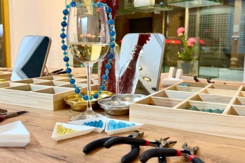 Een tafel met een wijnglas, kralen en gereedschap voor sieraden maken. 1
