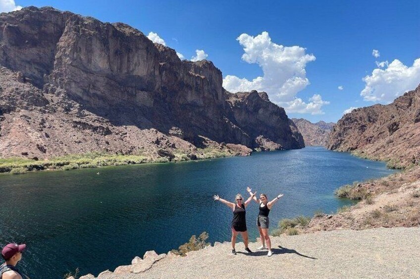 Dos personas de pie junto a un río con acantilados al fondo. 1