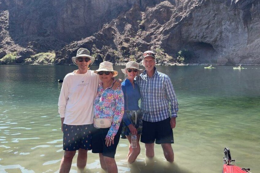 Cuatro personas de pie junto a un lago tranquilo con acantilados rocosos al fondo. 3