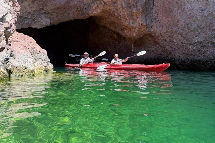 Dos personas remando en kayak rojo por aguas verdes y transparentes cerca de la entrada de una cueva rocosa. 4
