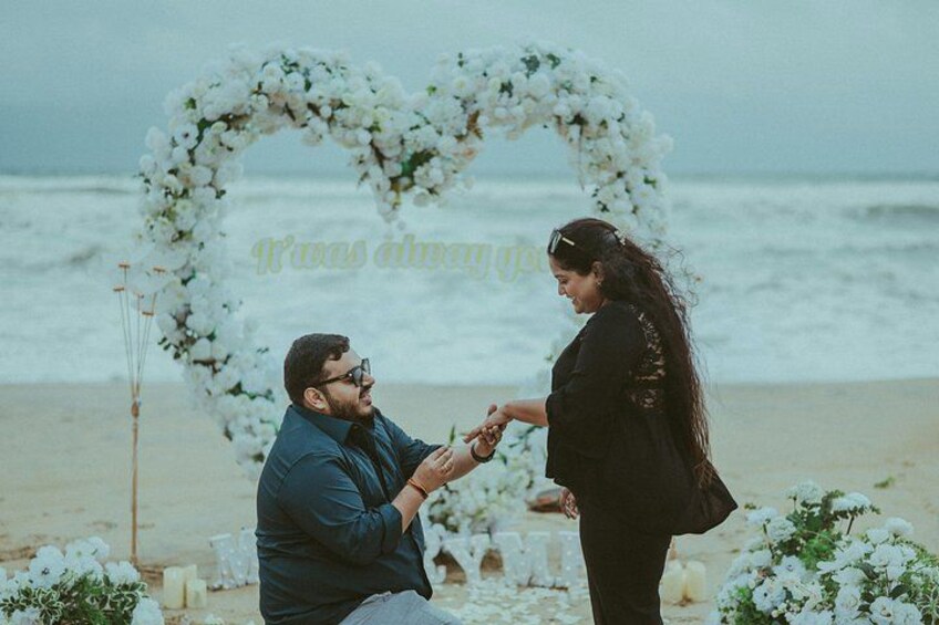 A beach wedding ceremony with a heart-shaped floral arch and a couple exchanging rings. 2