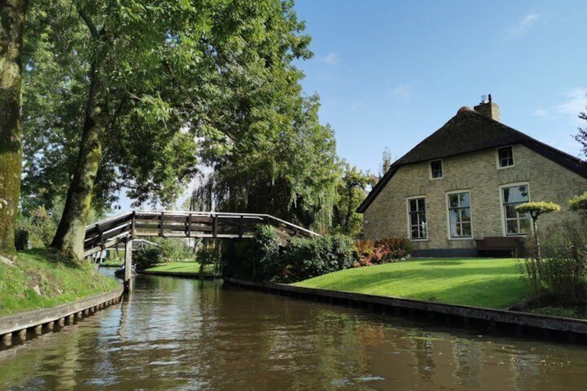 A stone house with a wooden bridge over a canal, surrounded by trees and a well-kept lawn. 5