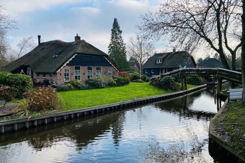 A canal with houses on either side, a wooden bridge, and a grassy area. 3