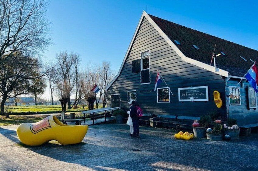 A wooden building with a sign reading 'De Zaanen Schans,' a yellow shoe-shaped sculpture, and Dutch flags. 4