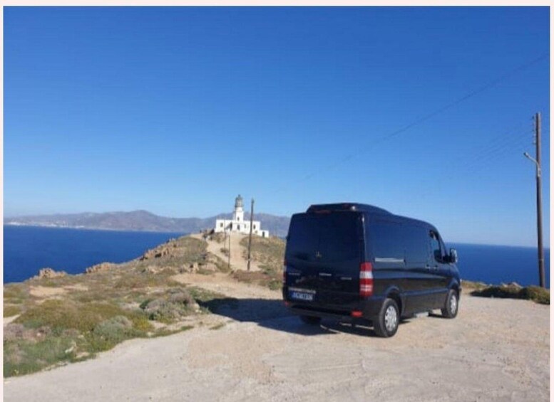 A black van parked on a dirt road with a lighthouse in the background. 4