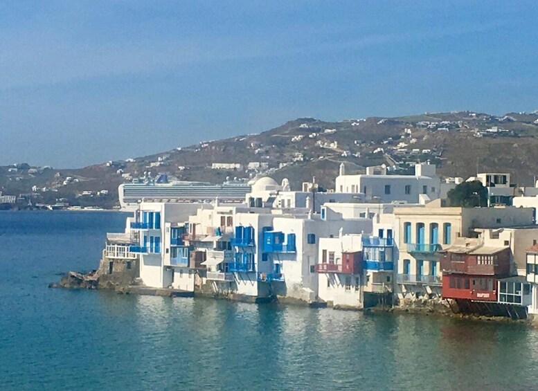A coastal village with white and blue buildings, a cruise ship in the background, and a hilly landscape. 3