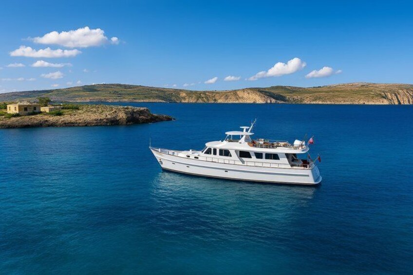 A white yacht on calm blue waters with a rocky coastline and clear sky in the background. 1