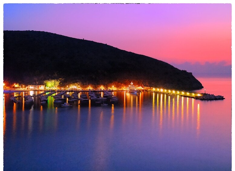A marina at dusk with boats docked, a pier extending into calm waters, and a hill in the background. 5