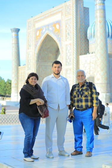 Three people standing in front of a large, ornate building with intricate patterns and a large archway. 1
