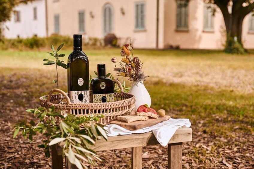Une table en bois installée à l’extérieur, sur laquelle on a disposé des bouteilles, un panier et un vase rempli de fleurs, pour un pique-nique. 5