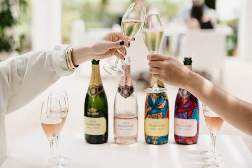 Eine Person hält ein Weinglas, im Hintergrund sind Weinflaschen und Champagnerflaschen zu sehen. 5